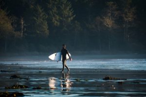 Man carrying a surfboard in Tofino on Vancouver Island - Photo by Spencer Watson