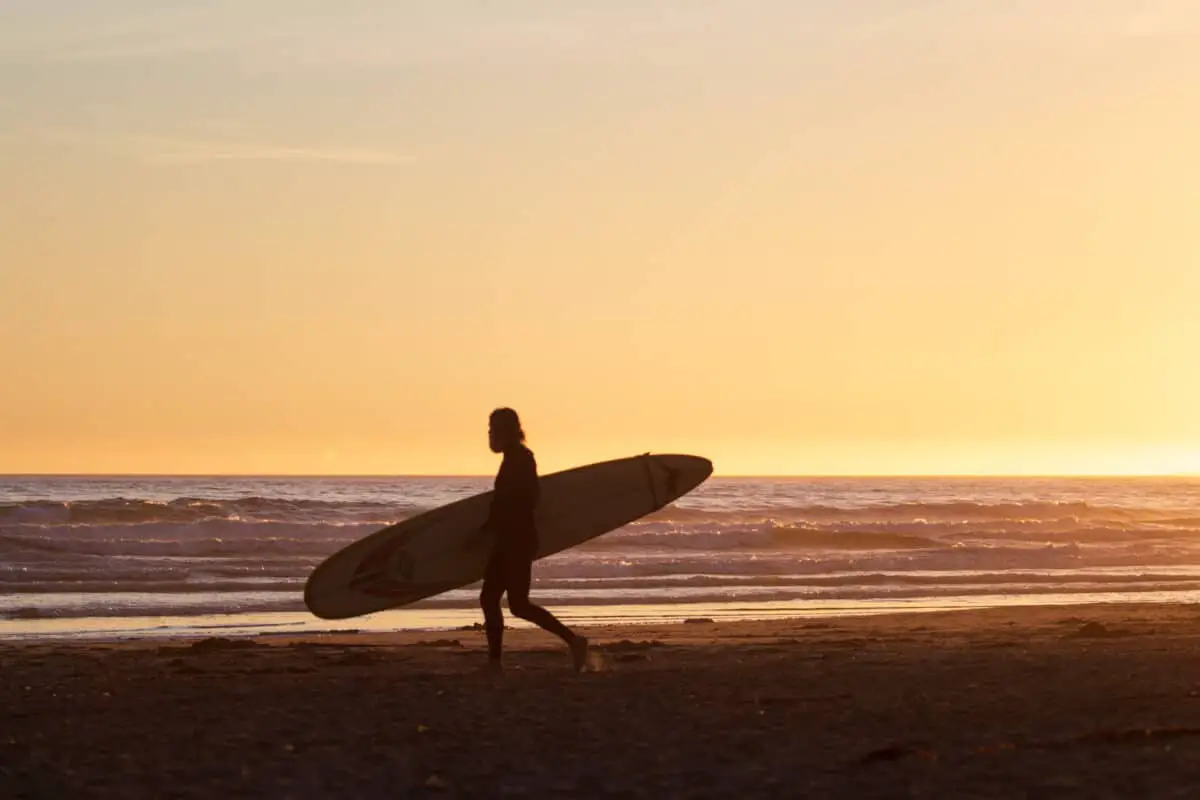 A surfer carrying their surfboard as the sun sets in Tofino