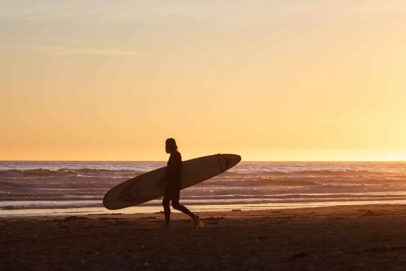 A surfer carrying their surfboard as the sun sets in Tofino