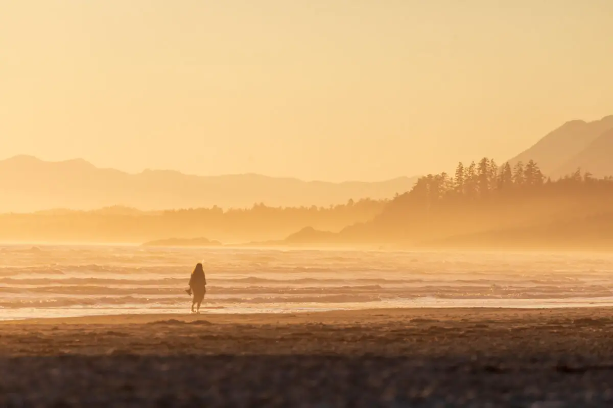 A woman walking in the surf of Wickaninnish Beach in Tofino, with ocean mist