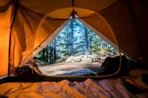Sleeping bag inside an open tent with a campfire
