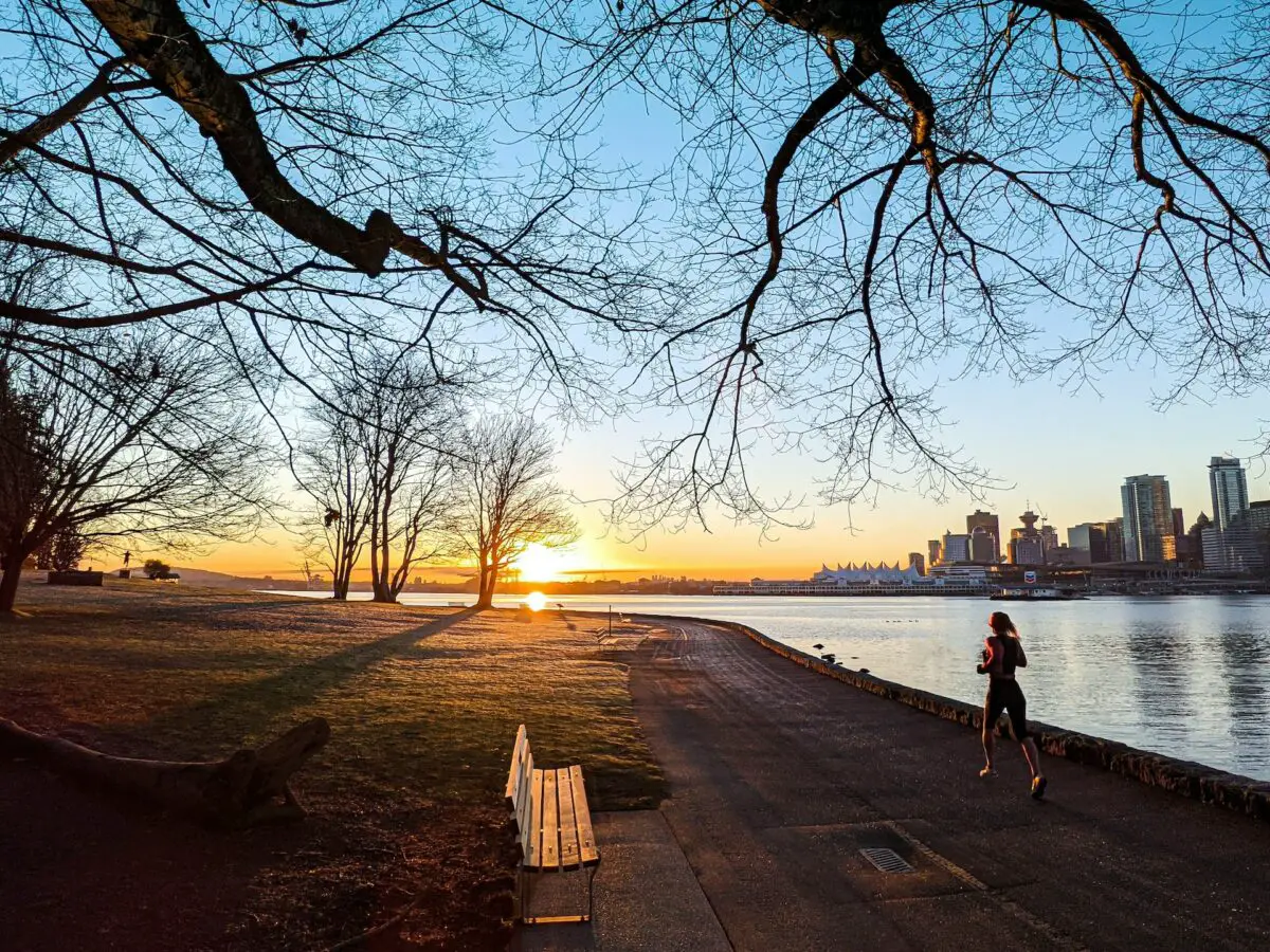 A woman going for a jog in Stanley Park as the sunrises over downtown Vancouver