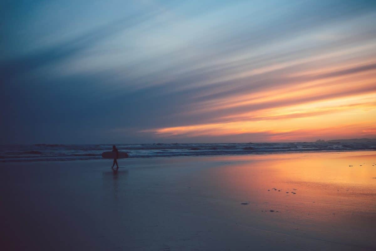 A surfer walking with their surfboard on a Tofino Beach at sunset